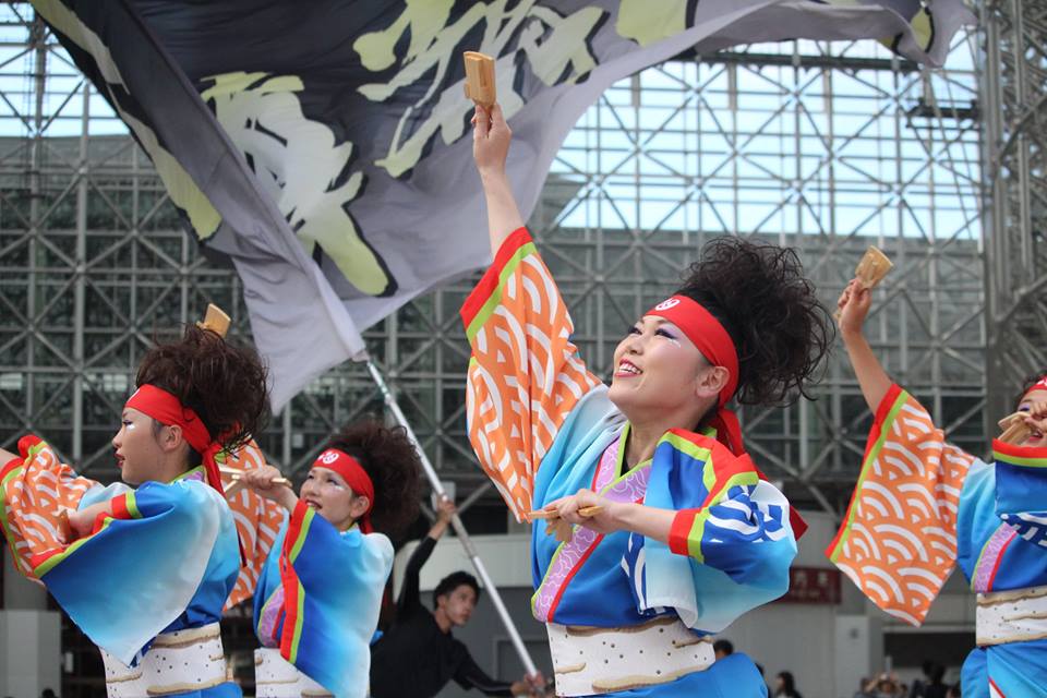 Yosakoi team with flags and clappers under Kanazawa Stations Motenashi Dome, by Tamaya Greenlee