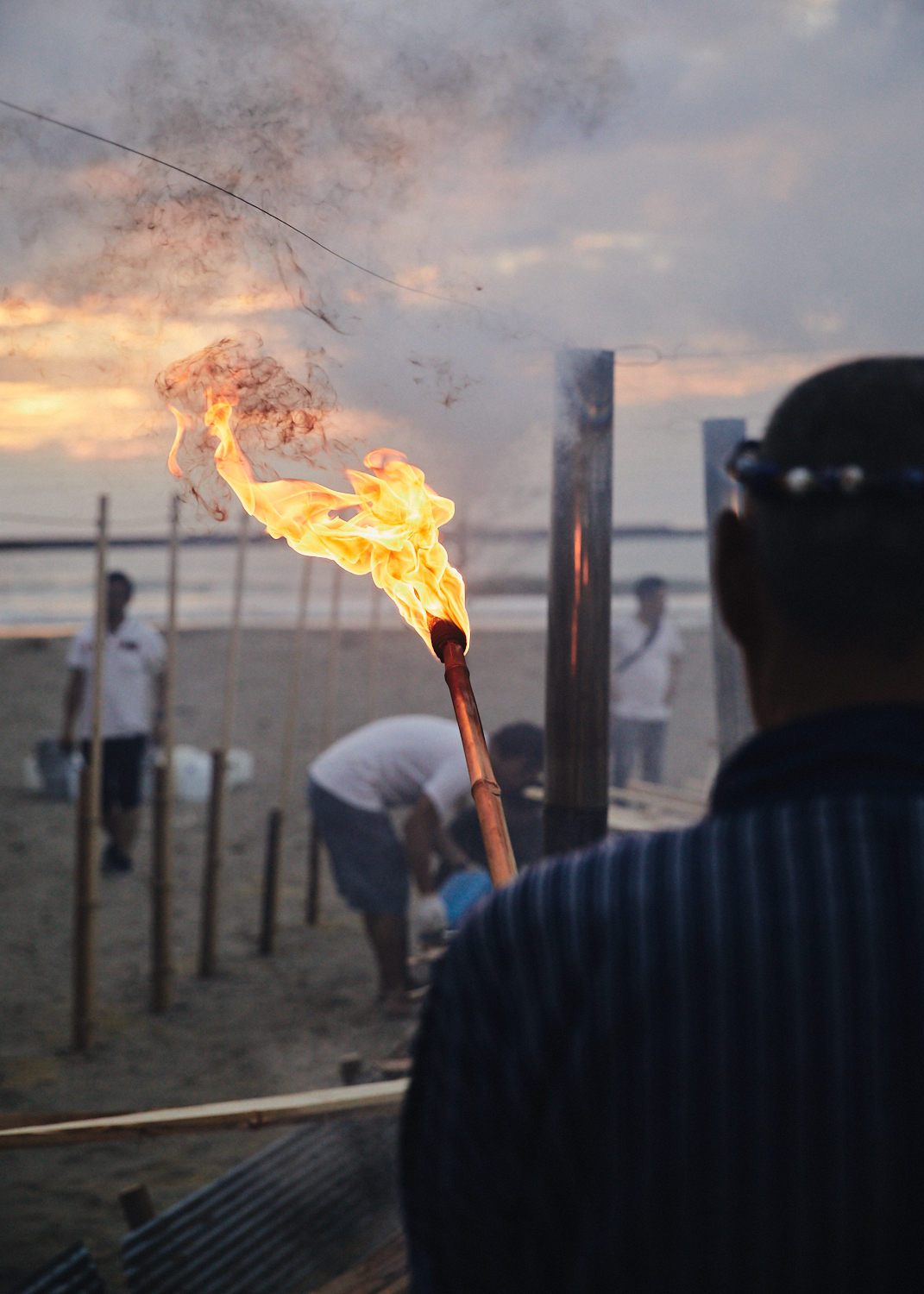 Master Iida brings a torch for the wood to turn the wild kiln into a bonfire.