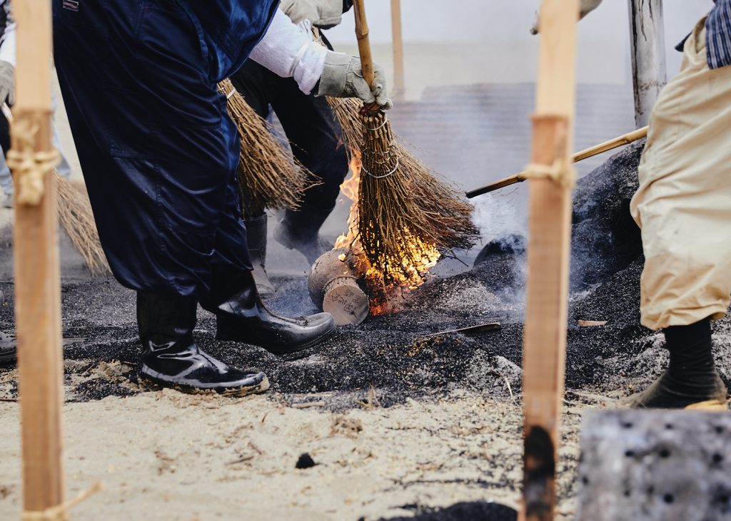 The brooms that brush the burning rice hulls catch fire as they reveal the completed earthenware pottery pieces.