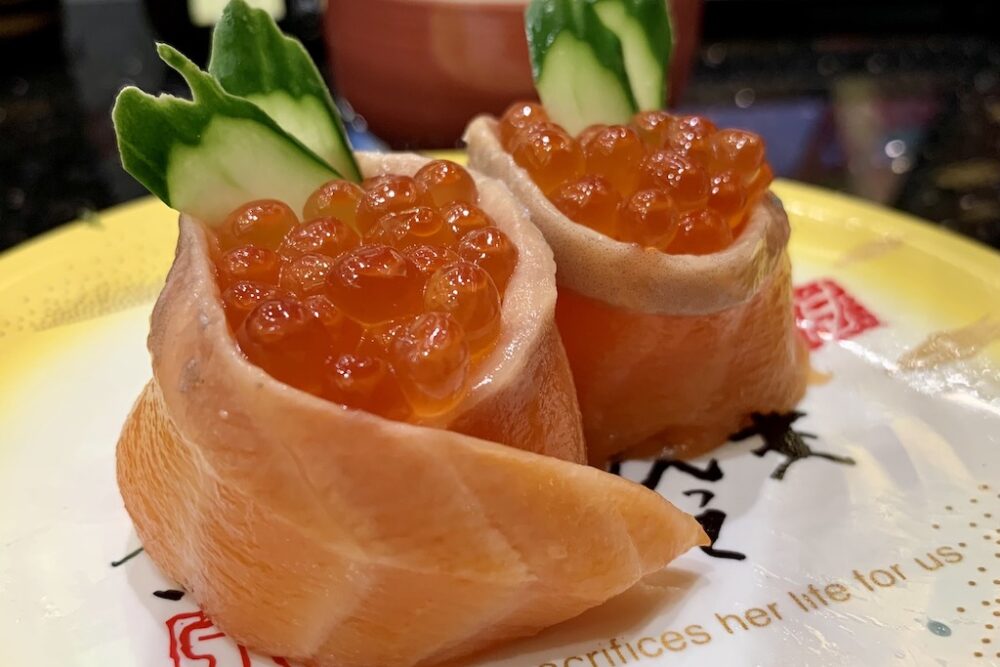 A specialty sushi roll called "parent and child salmon roll" on a plate that reads "Mom sacrifices her life for us"