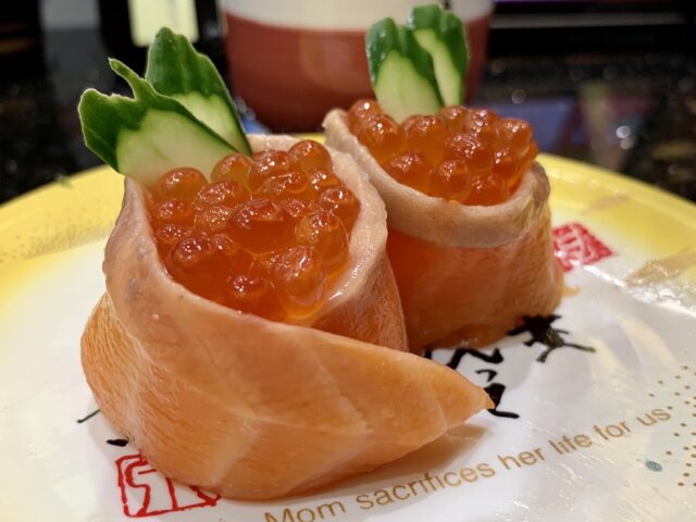 A specialty sushi roll called "parent and child salmon roll" on a plate that reads "Mom sacrifices her life for us"