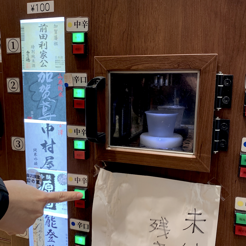 pressing a button to select the sake of choice to be poured into the cup by the sake vending machine at Anto in Kanazawa Station