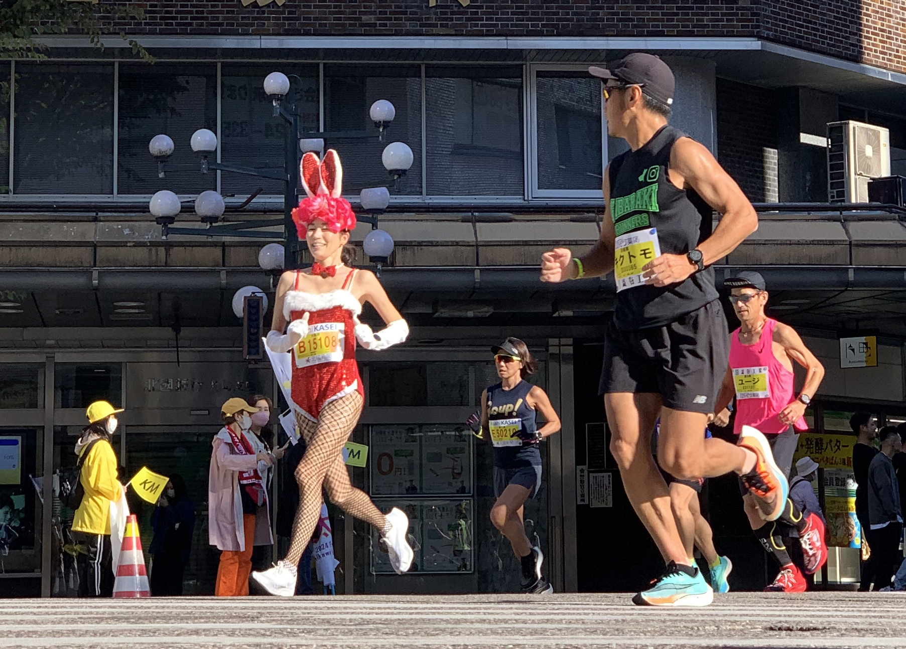 One runner at the Kanazawa Marathon watches another who is dressed up a bit like a Playboy Bunny
